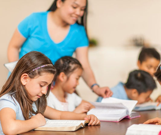 teacher with 4 children with Bibles open on a table